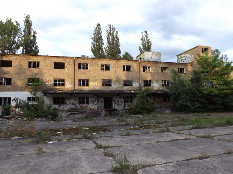 Verlassene Ruine eines langgezogenen 3 stöckigen Gebäudes an einem zugewachsenen Hof von Außen