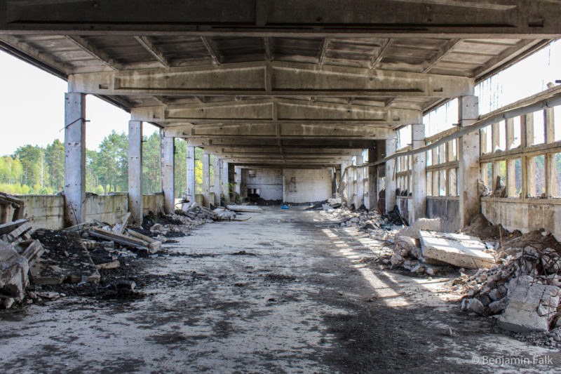 Das innere einer länglichen Betonhalle mit kaputten Seiten und umherliegenden Betontrümmern.