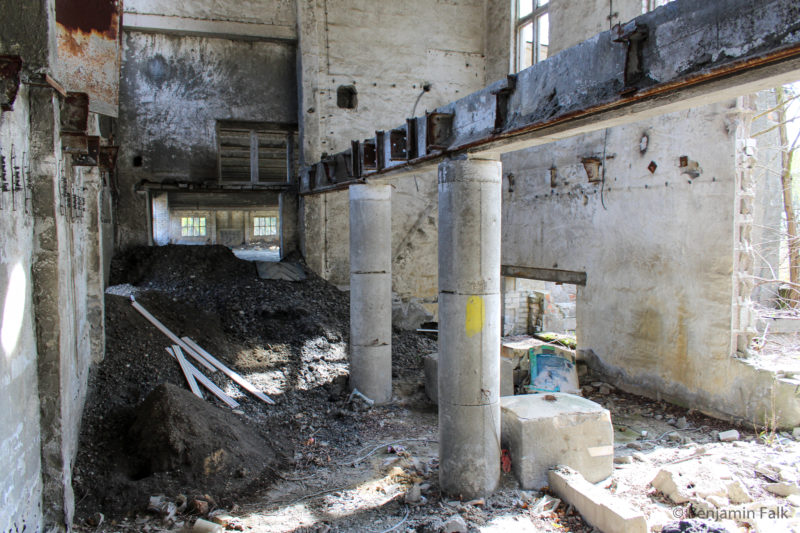 Nebenraum einer Beton-Lagerhalle mit aufgehäuften Erd-Hügel und einem Metallträger der von Betonsäulen getragen wird.