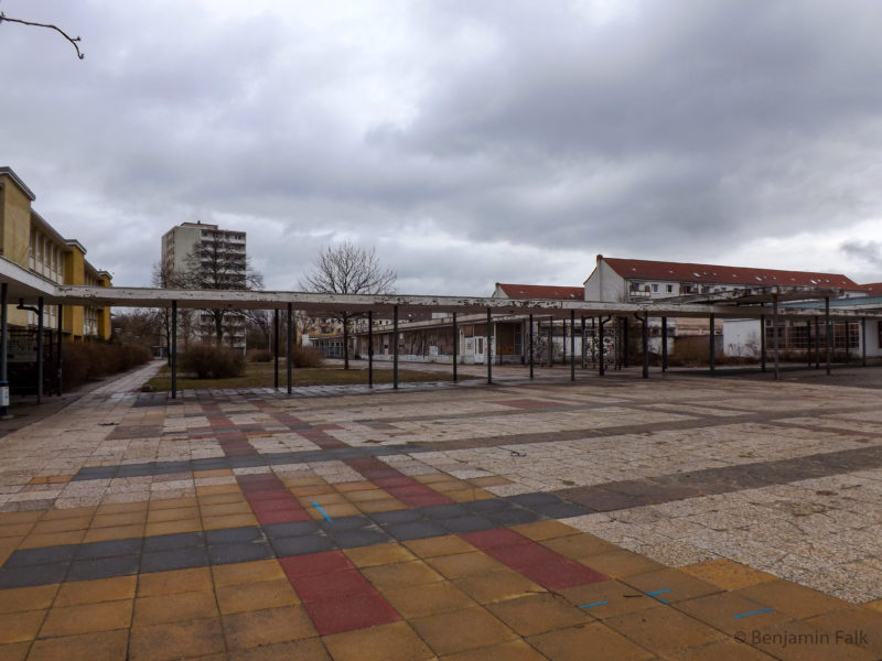 Platz der Jugend in Eisenhüttenstadt, mit Blick auf ein verlassenen und heruntergekommenen Nahkauf/Einkaufszentrum vor einem Hochhaus und.