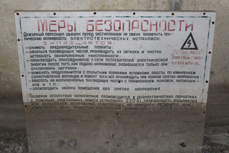 Elektro-Warnschild in russisch, dessen untere Hälfte drecküberzogen ist.