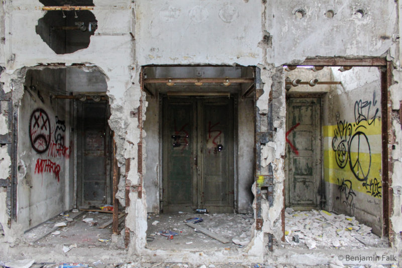 3 Ausgangstüren nebeneinander hinter jeweils einem Betondurchbruch mit frei liegenden Stahlträgern und Graffiti