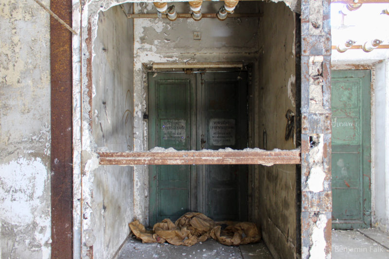 Tür fotografiert durch einen Betondurchbruch mit einem im Weg liegenden Stahlträger der Wand.