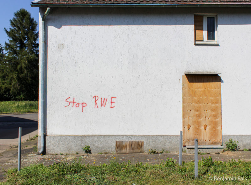 Weißes Haus mit vernagelten Türen und Fenstern und einem einzelnen Stop RWE-Graffito an der Wand.