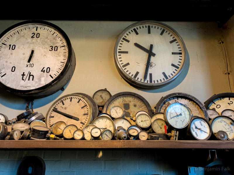 Verschiedene nicht-funktioneirende Uhren und Druckmesser in unterschiedlichen Zuständen und Verschmutzungsgraden auf einem Holz-Regalbrett.