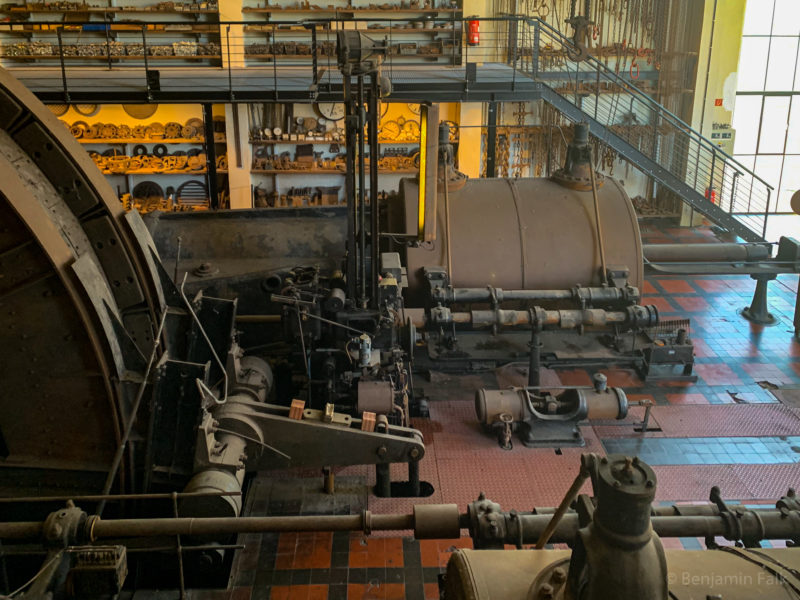 Stillgelegte Maschinenhalle mit großen Industriemaschinen von der Seite aus fotografiert mit Museumsstücken an der Rückwand.