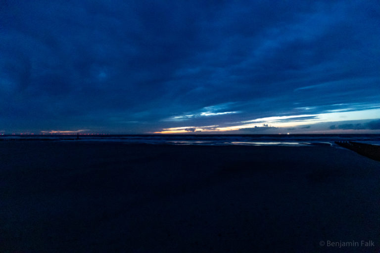 Meer vor einem leeren Strang bei Ebbe im Sonnenuntergang hinter Wolkenbändern.