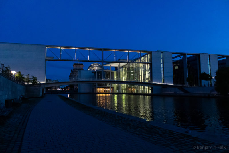 Spreebogen mit Blick auf die Bundestagsgebäude im Dämmerungslicht, mit Blick auf die beleuchtete Glasfront und die beleuchtete Brücke zwischen des Bundestagsgebäuden.