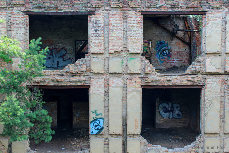 4 leere Fensterhöhlen mit Graffiti in den Räumen dahinter in einem verfallenen Backsteingebäude. (Beelitzer Heilstätten)