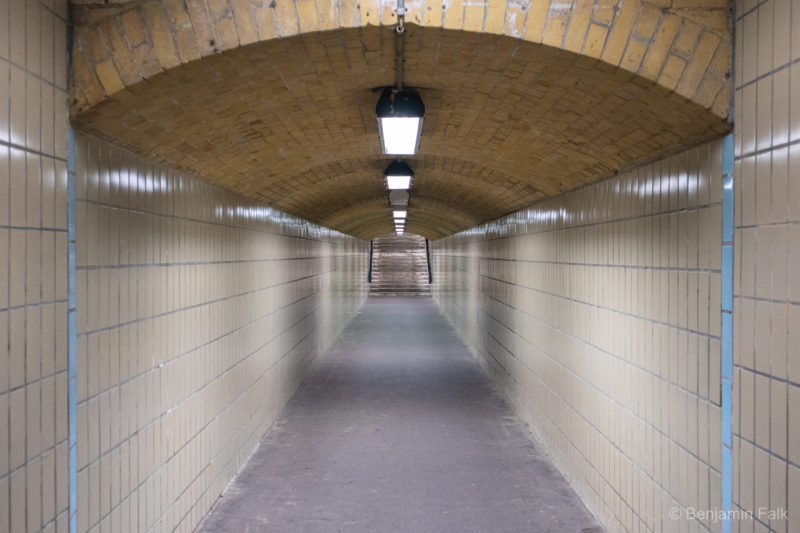 Blick in den beige gefliesten Fußgänger-Tunnel im S Wannsee mit gewölber gemauerter brauner Decke.