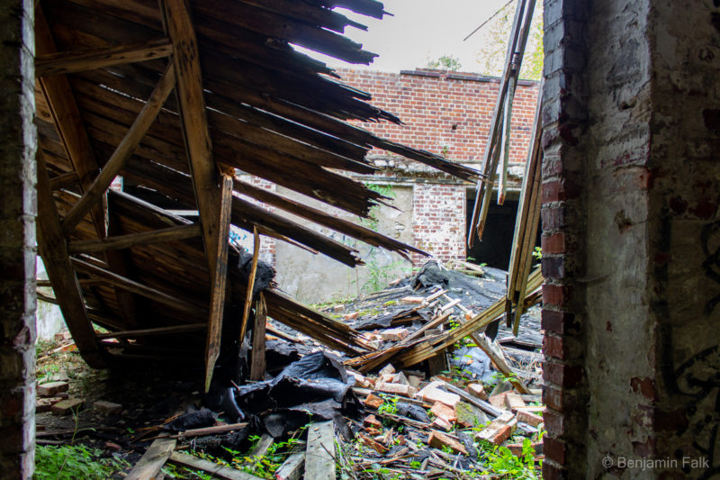 Innenhof einer Ruine mit eingestürztem Vordach, aus dem inneren des Gebäudes unter dem eingestürztem Dach hinweg fotografiert.