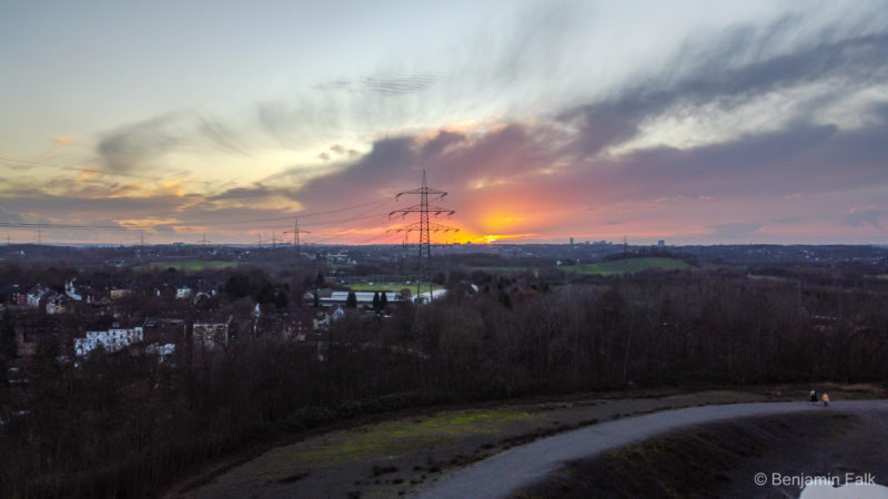 Sonnenuntergang über dem Ruhrgebiet, mit der rot durch eine Wolke scheinende Sonne, aufgenommen aus der Luft über der Halde Rheinelbe.