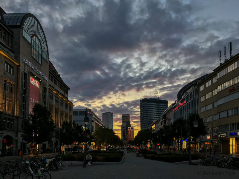 Aufnahme vom Berliner Wittenbergplatz die Tauentzienstr. runter Richtung Ku’damm. Blick an den Läden vorbei auf die Wolkenkratzer in der Abenddämmerung.